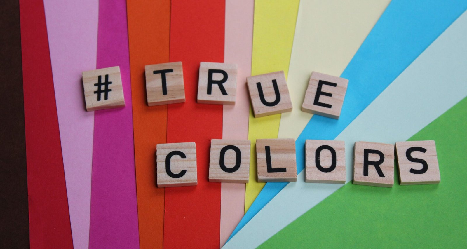 Mehrere Scrabble-Steine bilden das Wort 'True Colors' auf einer ebenen, hellen Oberfläche