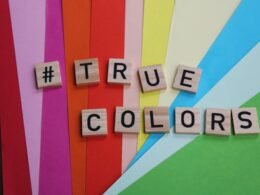 Mehrere Scrabble-Steine bilden das Wort 'True Colors' auf einer ebenen, hellen Oberfläche