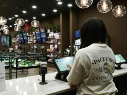 Kunde verwendet ein Tablet am Tresen eines Dispensary-Shops zur digitalen Bestellung und Beratung.