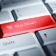 Roter 'Buy Now!' Button auf einer weißen Computertastatur als Symbol für Online-Shopping und E-Commerce