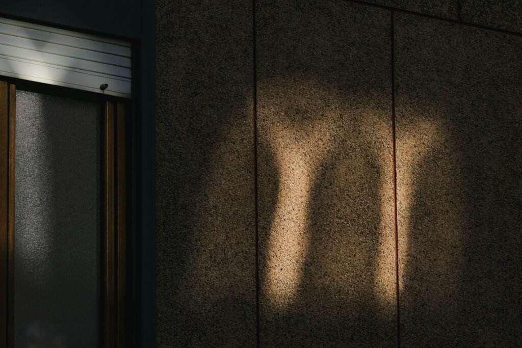 Schatten eines menschlichen Beins streckt sich deutlich auf einer hellen Wand, aufgenommen mit natürlichem Licht