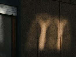 Schatten eines menschlichen Beins streckt sich deutlich auf einer hellen Wand, aufgenommen mit natürlichem Licht