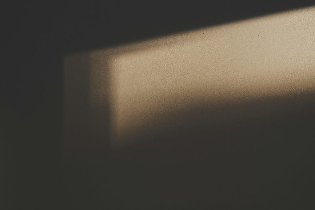Der Schatten eines rechteckigen Fensters fällt auf eine helle Wand und erzeugt geometrische Muster im Innenraum.