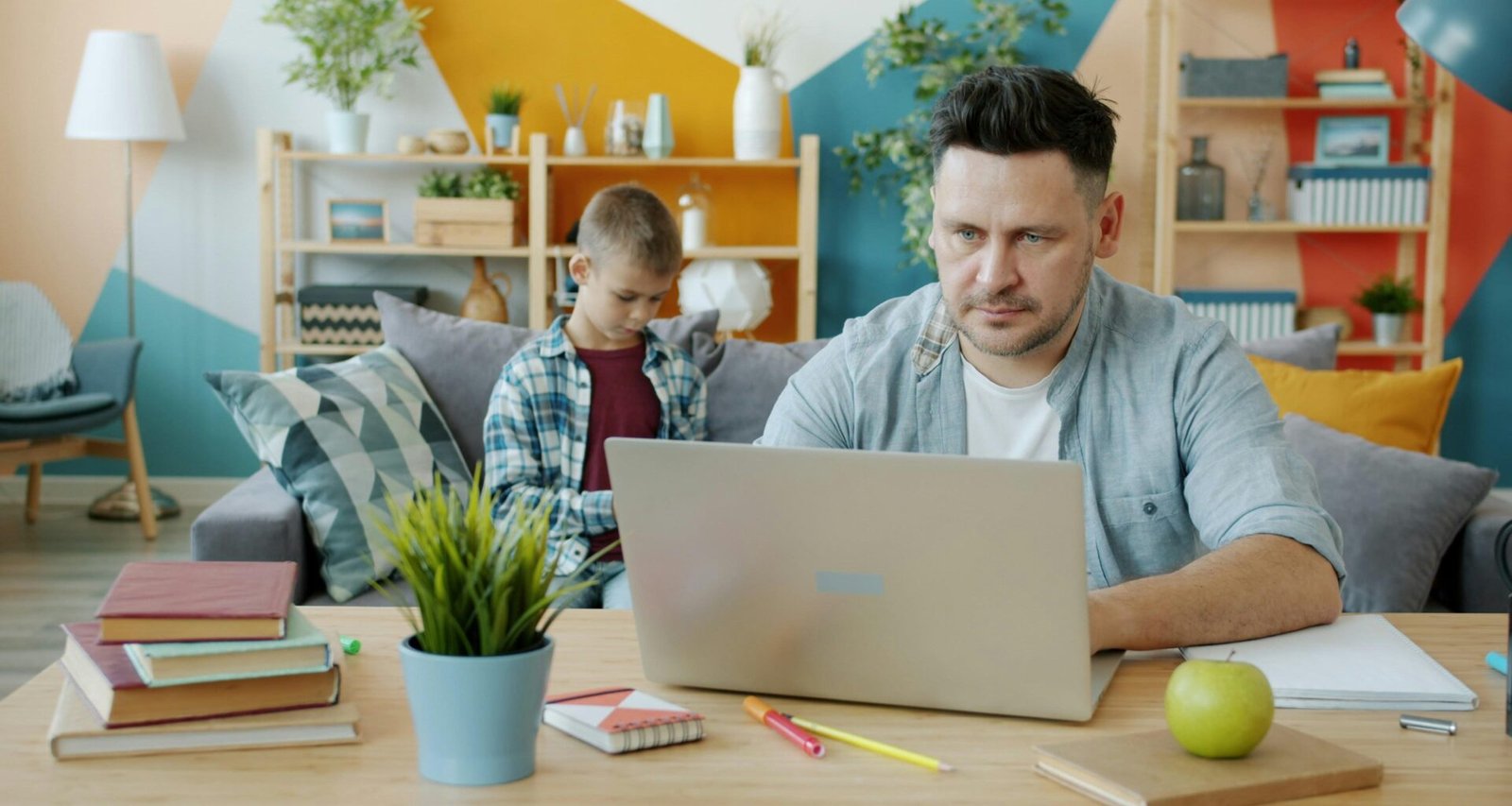 Vater arbeitet am Laptop, während sein Sohn auf dem Sofa sitzt und sein Smartphone nutzt. Foto von Vitaly Gariev.