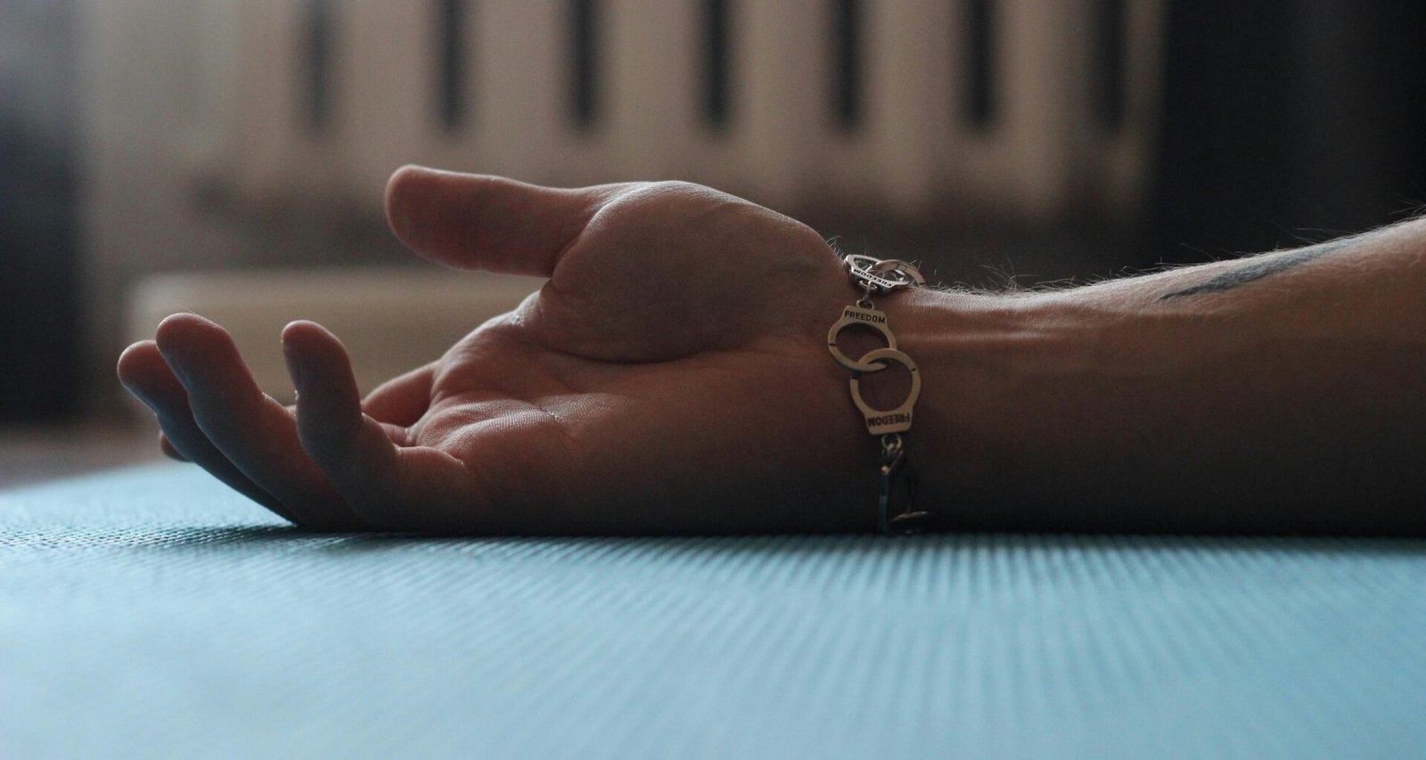 Eine Hand ruht auf einem Holztisch, im Hintergrund ist ein weißer Heizkörper sichtbar. Nahaufnahme im Innenraum.