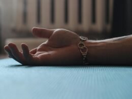 Eine Hand ruht auf einem Holztisch, im Hintergrund ist ein weißer Heizkörper sichtbar. Nahaufnahme im Innenraum.