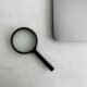 Eine Lupe liegt neben einem aufgeklappten Laptop auf einem Tisch, ideal für Themen rund um Recherche oder SEO-Analyse.
