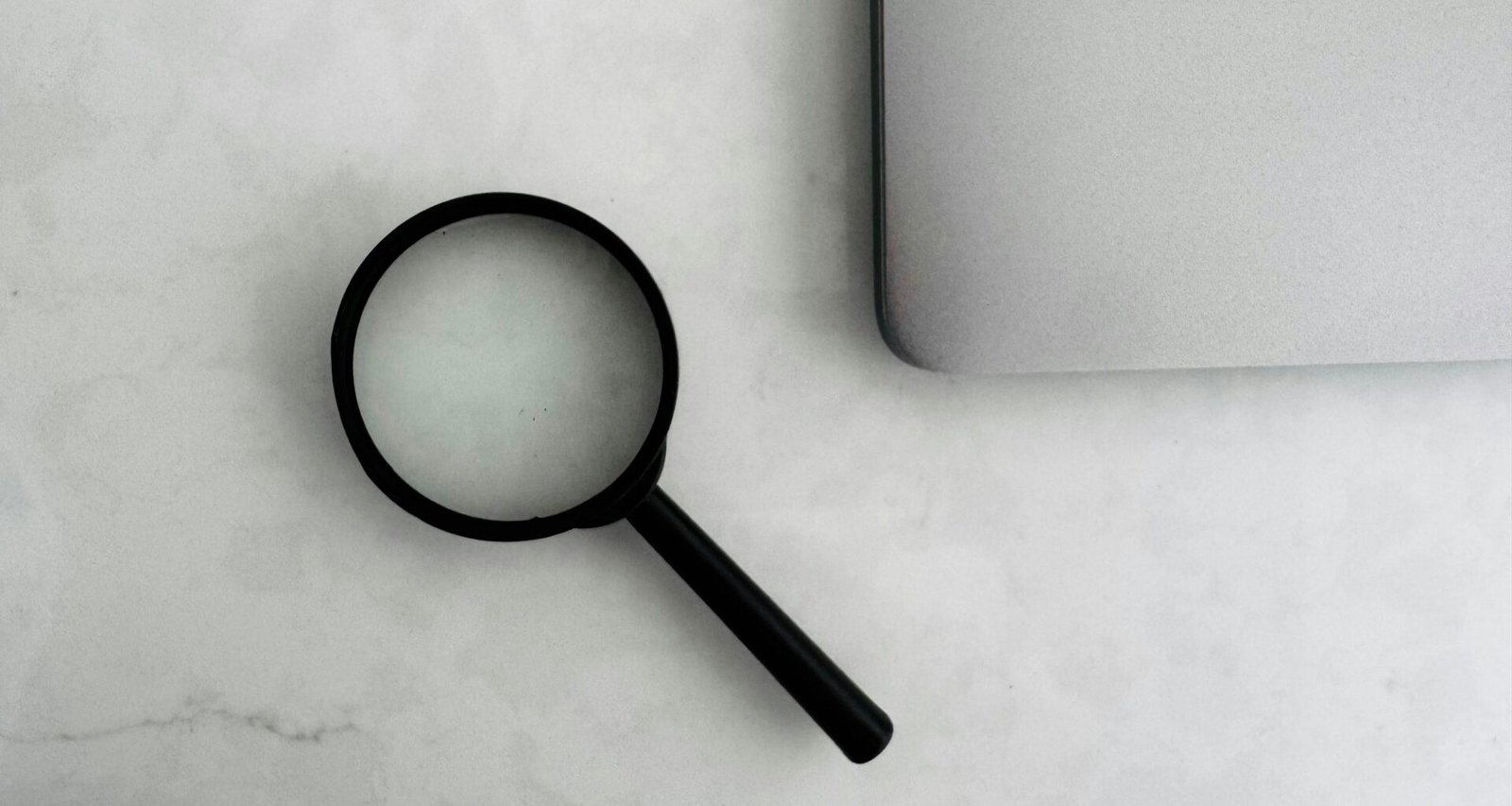 Eine Lupe liegt auf einem Tisch in der Nähe eines aufgeklappten Laptops, ideal für Artikel über Recherche oder Online-Marketing.