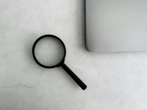 Lupe neben einem aufgeklappten Laptop auf einem Holztisch, Fokus auf Tools für Online-Analyse und SEO-Strategien.