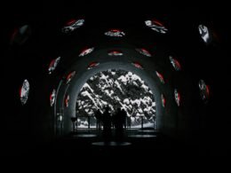 Mehrere Personen gehen durch einen Tunnel mit Wänden, auf die digitale Bilder und visuelle Projektionen geworfen werden.