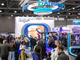 Besucher schlendern auf einer Ausstellung durch eine Messehalle mit zahlreichen Ständen und digitalen Displays.