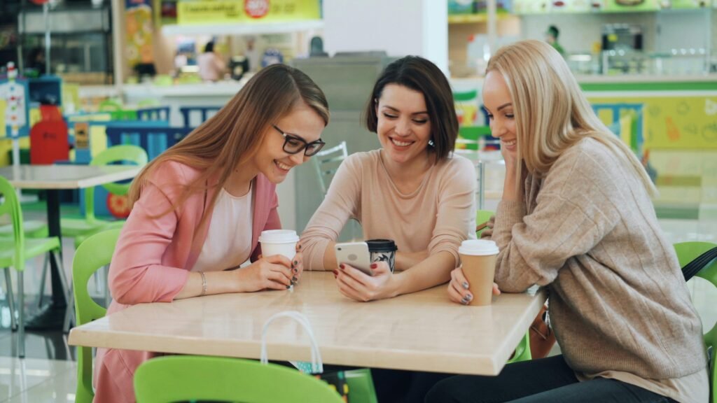 Drei Frauen sitzen in einem Café und schauen gemeinsam auf ein Smartphone am Tisch.
