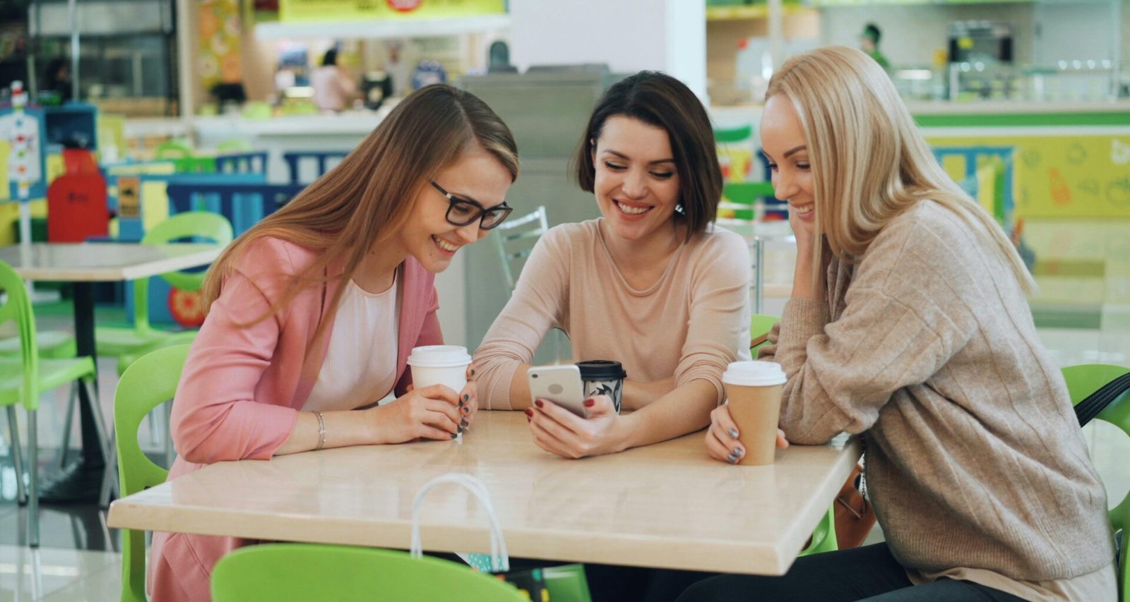 Drei Frauen sitzen in einem Café und schauen gemeinsam auf ein Smartphone am Tisch.