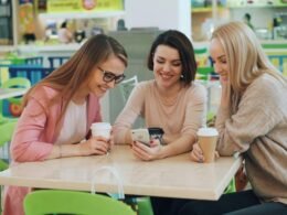Drei Frauen sitzen in einem Café und schauen gemeinsam auf ein Smartphone am Tisch.