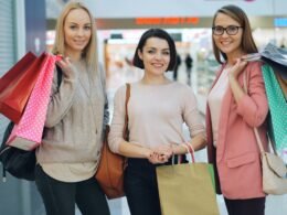 Drei Frauen halten Einkaufstaschen und gehen zusammen durch die Ladenpassage eines modernen Einkaufszentrums.