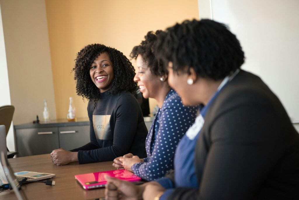 Drei Frauen unterhalten sich an einem hölzernen Konferenztisch in einem modernen Büro