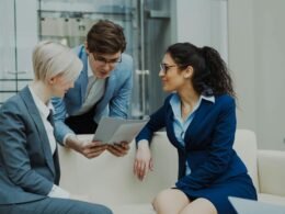 Drei Geschäftsleute in Anzügen sitzen zusammen und diskutieren Dokumente in einem hellen Büro