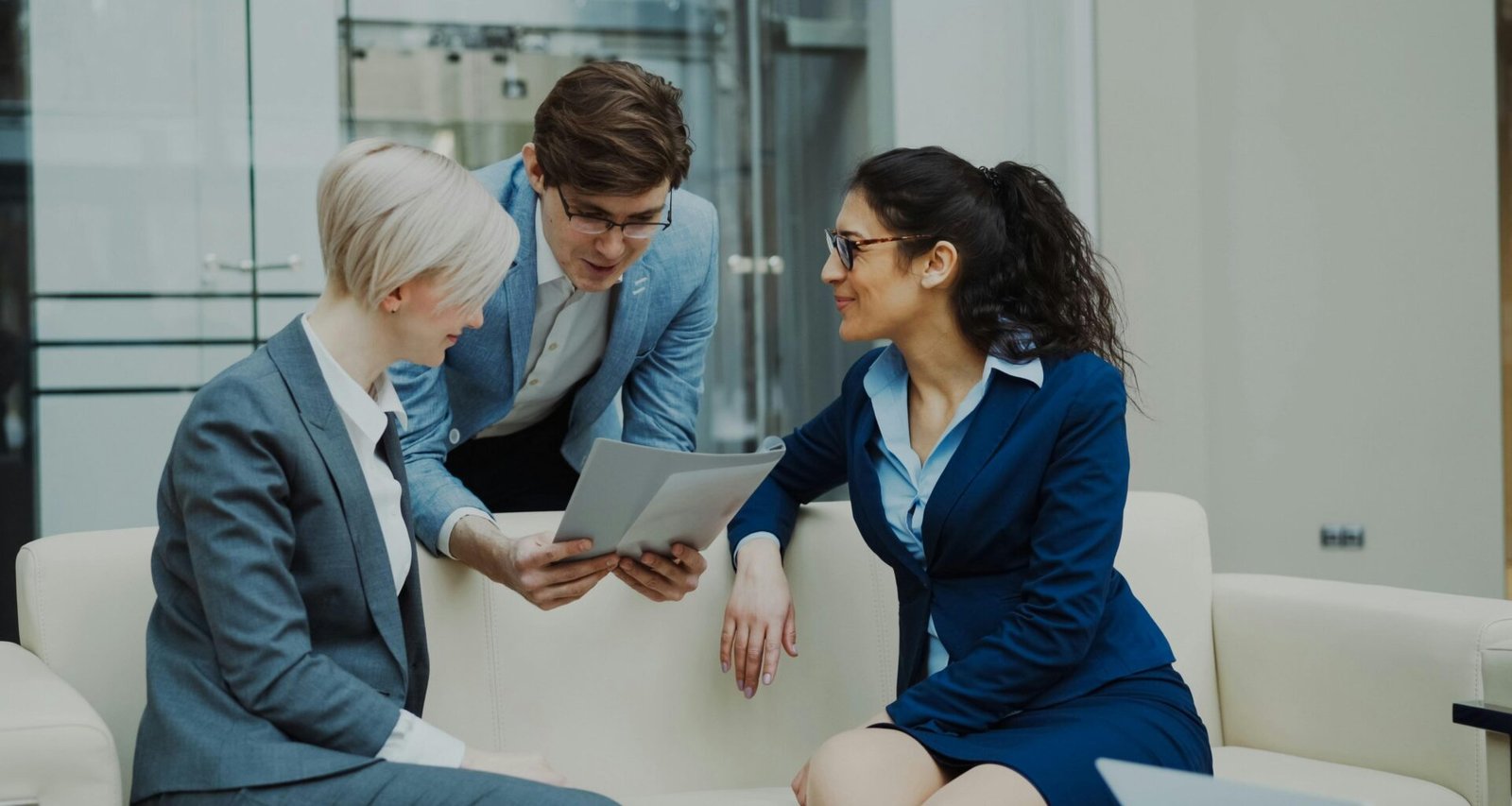 Drei Personen im Anzug sitzen am Konferenztisch und besprechen gemeinsam Dokumente in einem modernen Büro