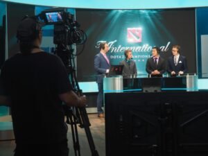 Drei Männer in Anzügen werden bei einem Dota 2 E-Sport-Event für eine Übertragung gefilmt