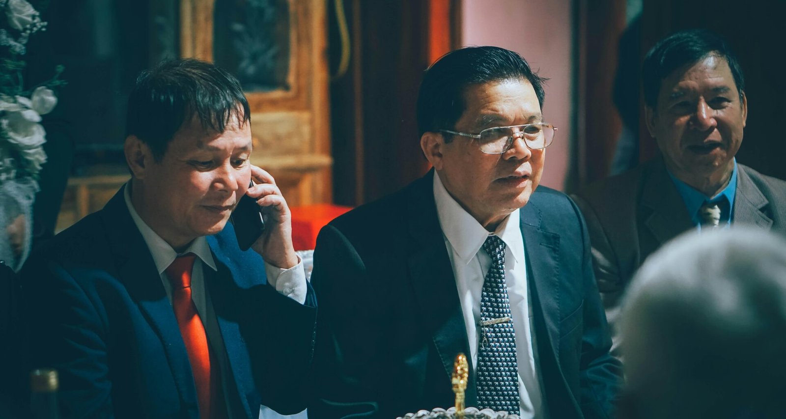 Drei Männer in Anzügen stehen bei einer formellen Zusammenkunft und unterhalten sich in geschäftlicher Atmosphäre.