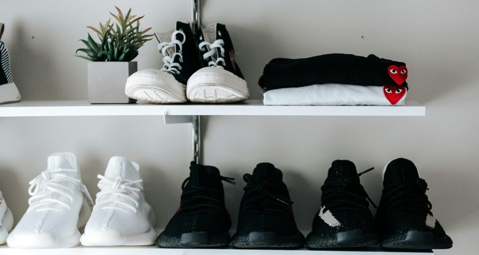 Drei Paar schwarze und weiße Schuhe auf einem schwebenden Regal, minimalistisch angeordnet vor einer neutralen Wand