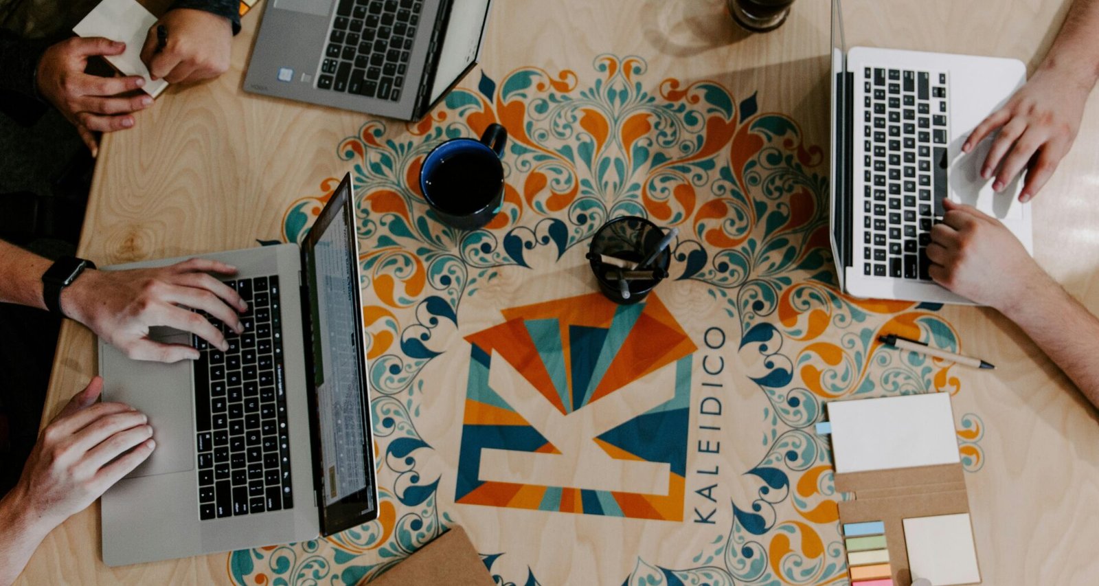 Drei Personen sitzen an einem Tisch und nutzen Laptops zur Zusammenarbeit in einem modernen Büro.