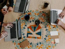 Drei Personen sitzen an einem Tisch und nutzen Laptops zur Zusammenarbeit in einem modernen Büro.