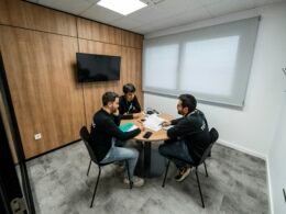 Drei Menschen bei einem Meeting in einem Konferenzraum mit Glaswänden und Tageslicht, aufgenommen während einer Besprechung