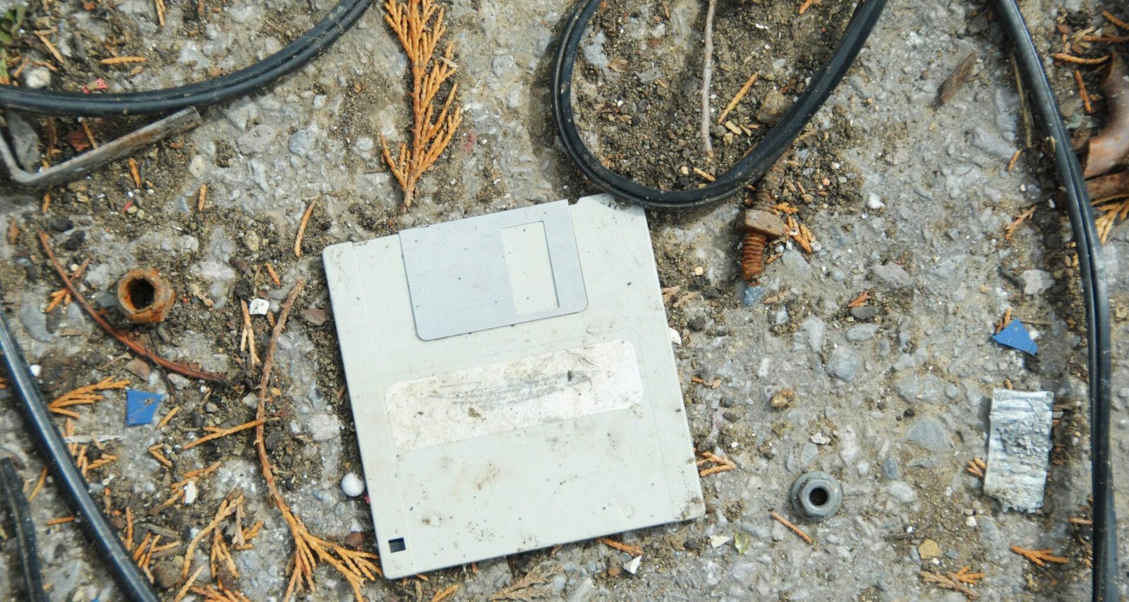 Ein alter Computer auf dem Boden, umgeben von verschiedenen Kabeln und Technikzubehör, erinnert an frühere Computerzeiten.