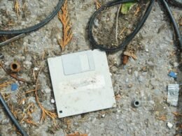 Ein alter Computer auf dem Boden, umgeben von verschiedenen Kabeln und Technikzubehör, erinnert an frühere Computerzeiten.