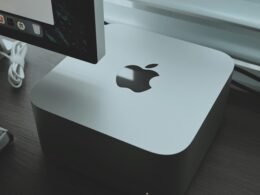 Apple Computer steht auf einem Holzschreibtisch in moderner Büroumgebung mit hellem Tageslicht.
