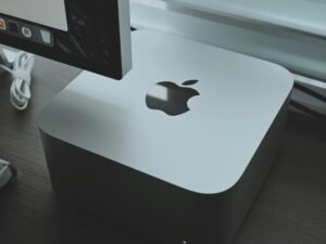 Apple Computer steht auf einem Holzschreibtisch in moderner Büroumgebung mit hellem Tageslicht.