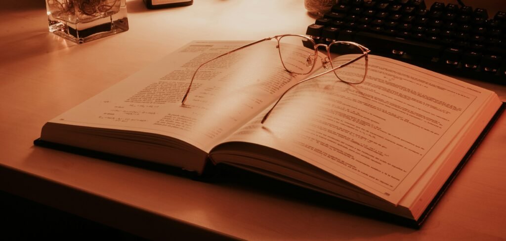 Ein offenes Buch mit einer klassischen Brille darauf, liegend auf einem Tisch, Symbol für Lernen und Wissen.