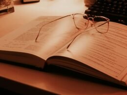 Ein offenes Buch mit einer klassischen Brille darauf, liegend auf einem Tisch, Symbol für Lernen und Wissen.