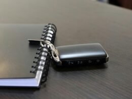 Ein Autoschlüssel und ein Notizbuch liegen auf einer hellen Oberfläche nebeneinander, deutliche Details beider Objekte sind erkennbar.