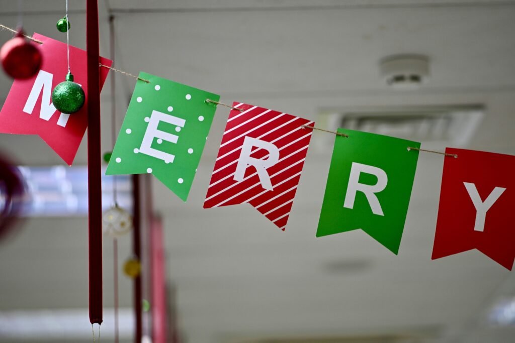 Ein Banner aus bunten einzelnen Fahnen mit der Aufschrift Merry Christmas hängt an einer Wand als Weihnachtsdekoration.