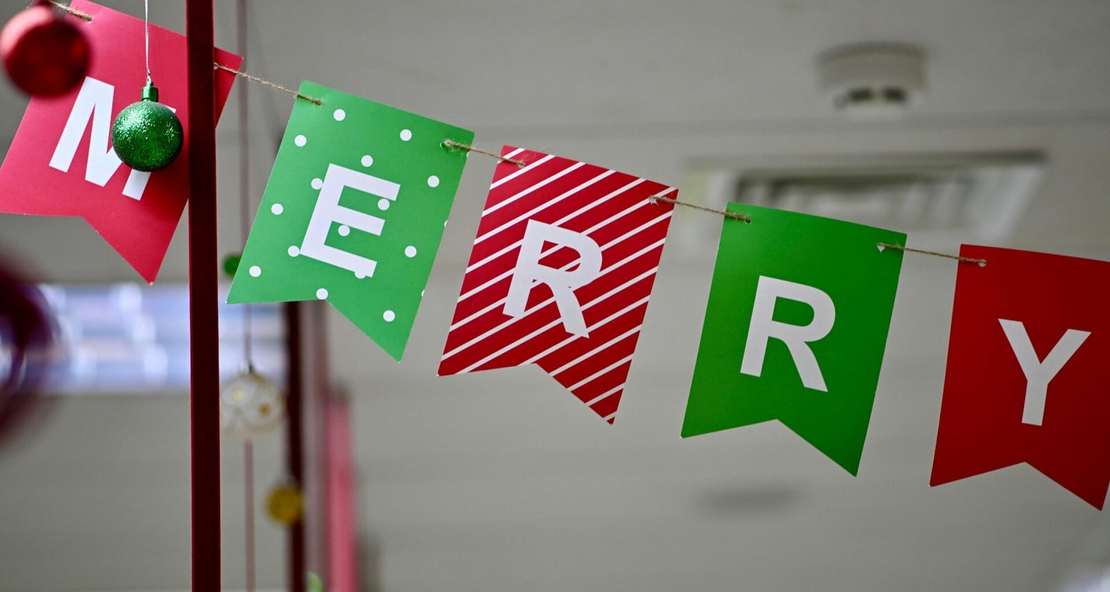 Ein Banner aus bunten einzelnen Fahnen mit der Aufschrift Merry Christmas hängt an einer Wand als Weihnachtsdekoration.