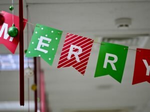 Ein Banner aus bunten einzelnen Fahnen mit der Aufschrift Merry Christmas hängt an einer Wand als Weihnachtsdekoration.