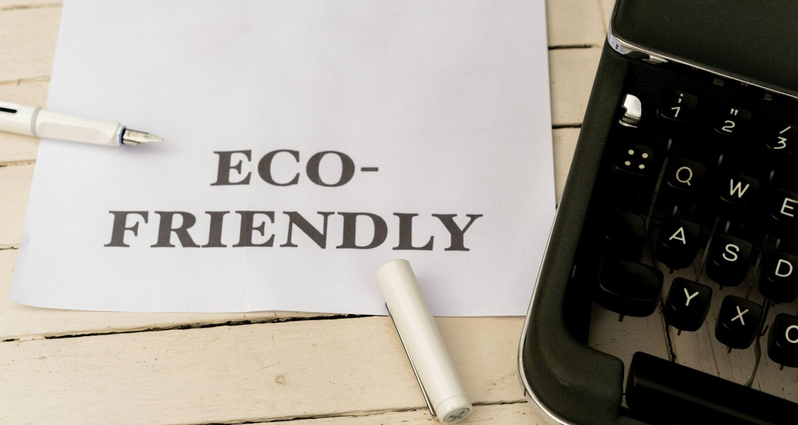 Papier mit der Aufschrift eco-friendly neben einer Schreibmaschine auf einem Holztisch, Symbol für nachhaltige Büroarbeit
