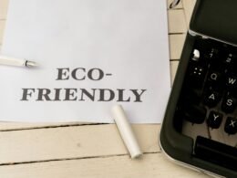 Papier mit der Aufschrift eco-friendly neben einer Schreibmaschine auf einem Holztisch, Symbol für nachhaltige Büroarbeit