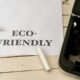 Papier mit der Aufschrift eco-friendly neben einer Schreibmaschine auf einem Holztisch, Symbol für nachhaltige Büroarbeit