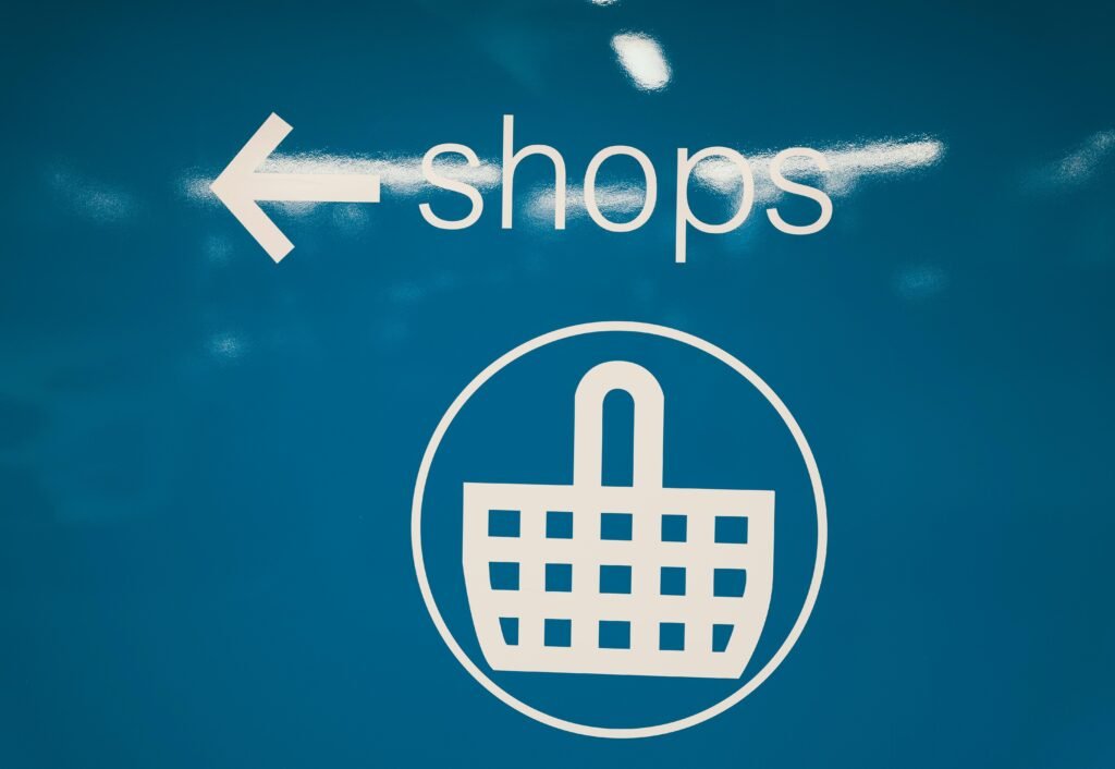 Blaues Schild mit weißem Einkaufskorb-Symbol vor schlichtem Hintergrund, als Piktogramm für Einkaufen oder Online-Shops geeignet.