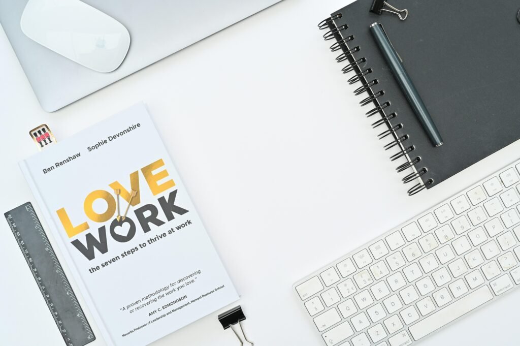 Ein Buch liegt auf einem Schreibtisch direkt neben einer Computertastatur, typischer Arbeitsplatz im Büroalltag.