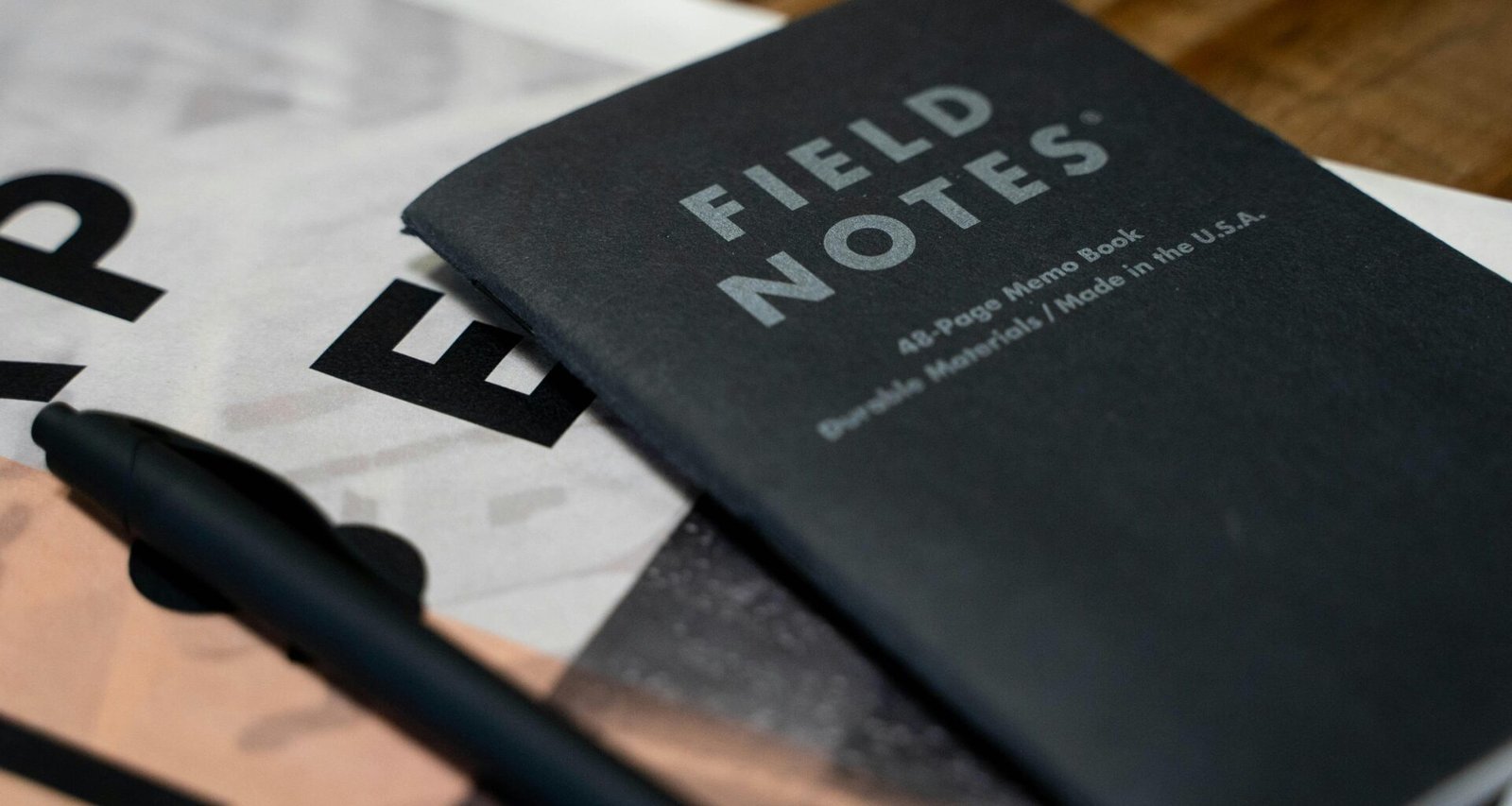 Ein auf einem Tisch liegendes Buch mit einem quer darüber platzierten Stift, bereit für Notizen oder kreative Einträge.