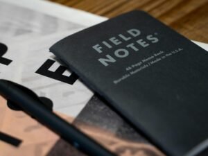 Ein auf einem Tisch liegendes Buch mit einem quer darüber platzierten Stift, bereit für Notizen oder kreative Einträge.