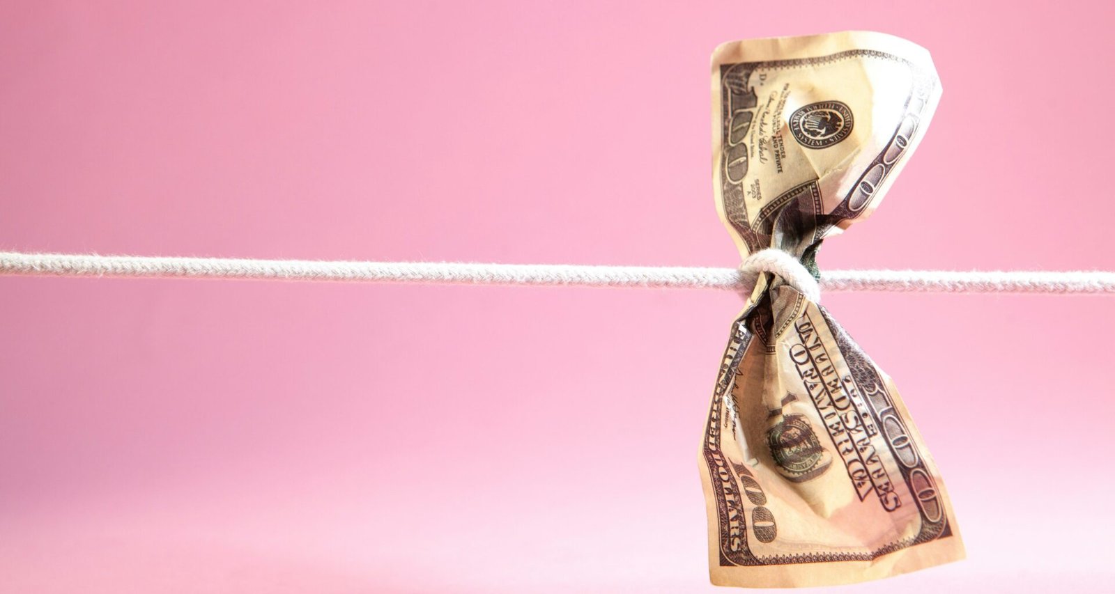 Ein Dollar-Geldschein ist an einer weißen Schnur verknotet, fotografiert vor neutralem Hintergrund.