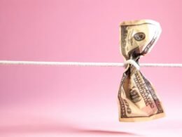 Ein Dollar-Geldschein ist an einer weißen Schnur verknotet, fotografiert vor neutralem Hintergrund.