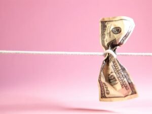 Ein Dollar-Geldschein ist an einer weißen Schnur verknotet, fotografiert vor neutralem Hintergrund.