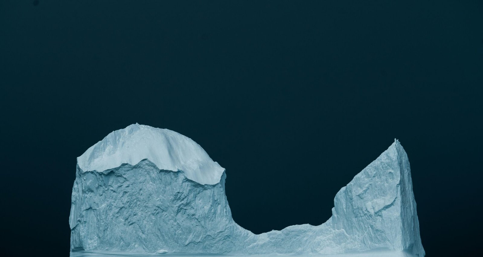 Ein großer Eisberg schwimmt auf der dunkelblauen Wasseroberfläche des Ozeans, aufgenommen aus der Ferne.