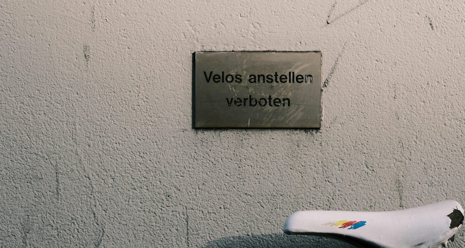 Fahrrad steht neben einer Mauer mit gut sichtbarem Schild, aufgenommen in einem städtischen Umfeld
